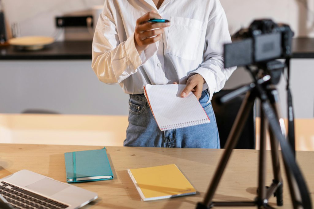 A content creator recording with a camera beside a laptop and notes